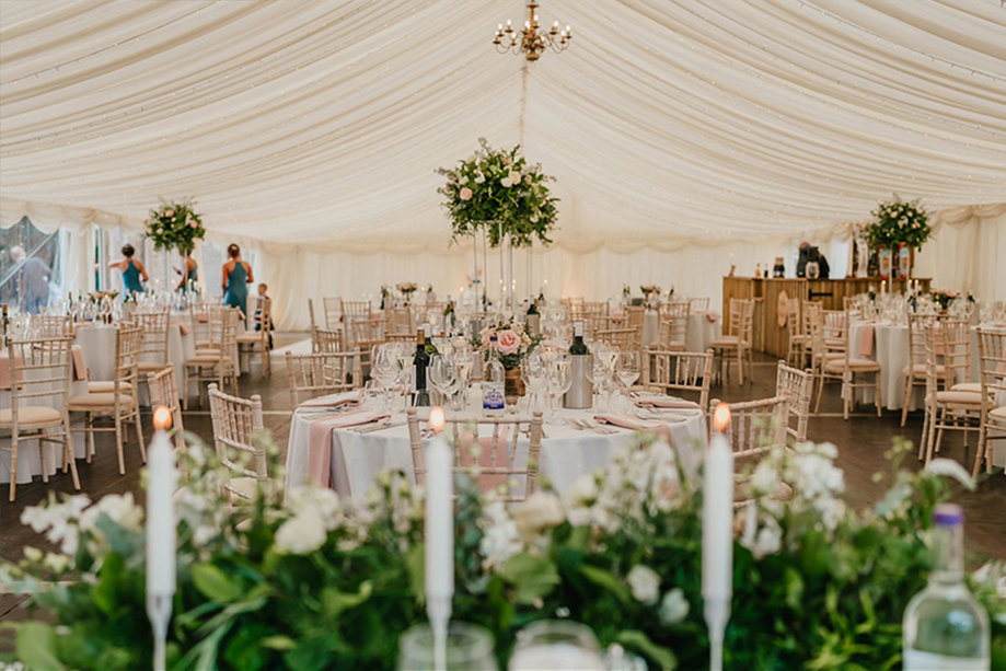 Inside a marquee set up for a wedding dinner with candles and foliage on the tables