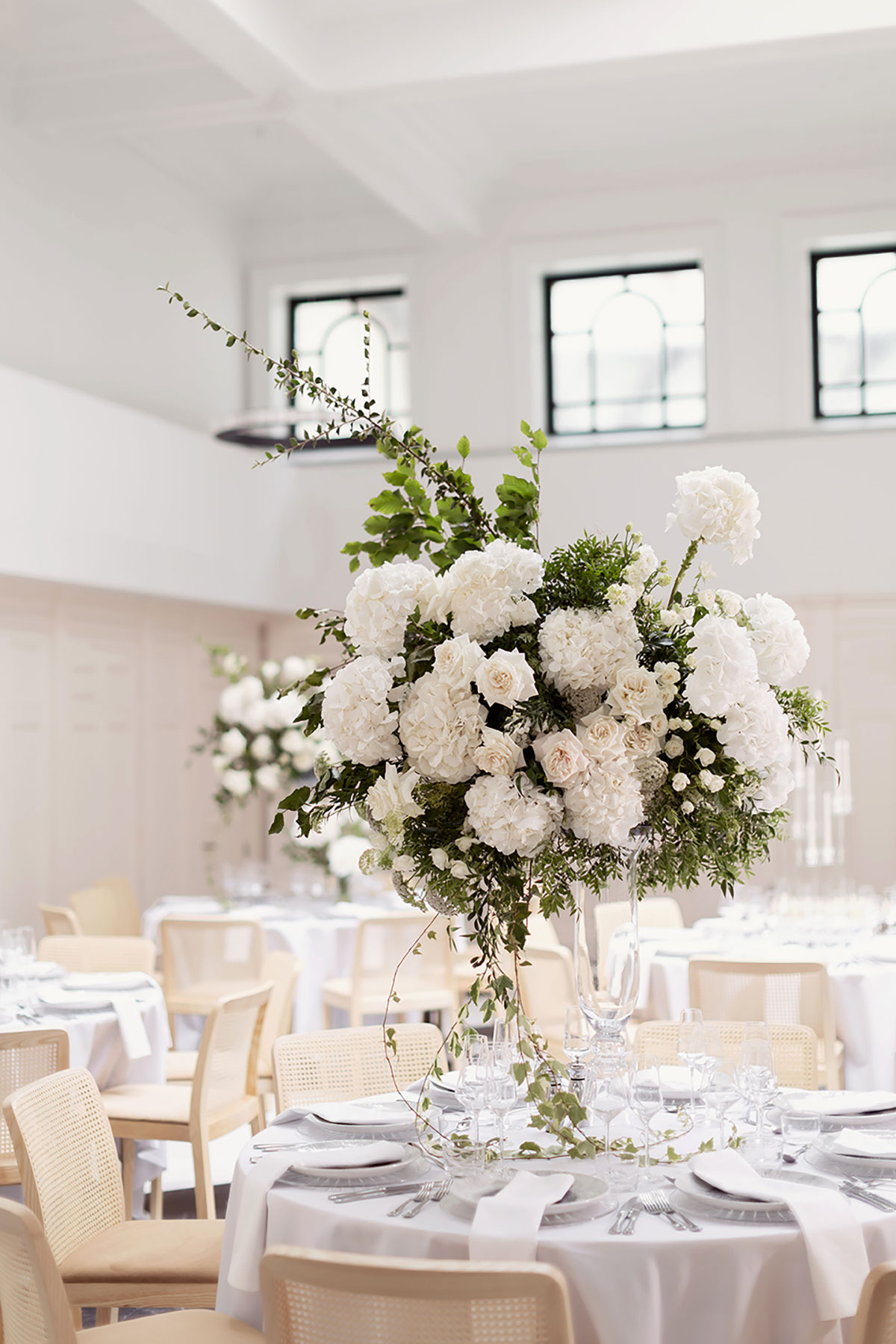 Tall glass vase filled with lush white hydrangeas and roses, styled as an elegant wedding table centrepiece