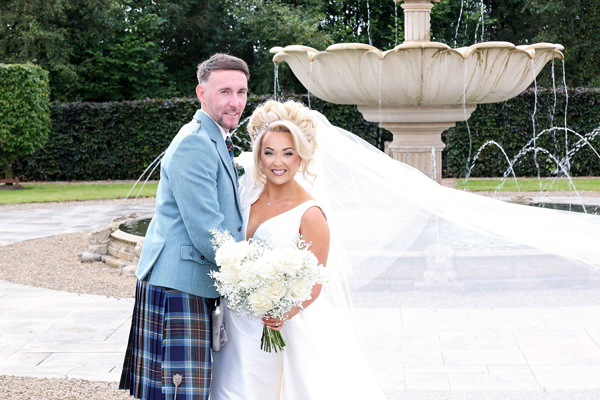 bride's veil floats in the wind as she smiles for photograph with groom during wedding at Ingliston Estate