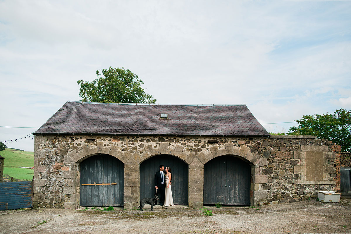 Couple standing beneath arched barn doors at Cormiston Farm wedding venue in the Scottish Borders.
