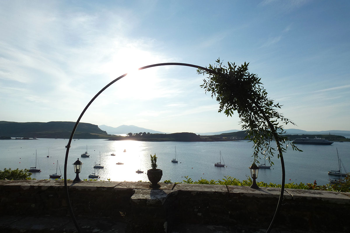 Circular metal wedding arch overlooking a Scottish harbour with boats on the water at sunset