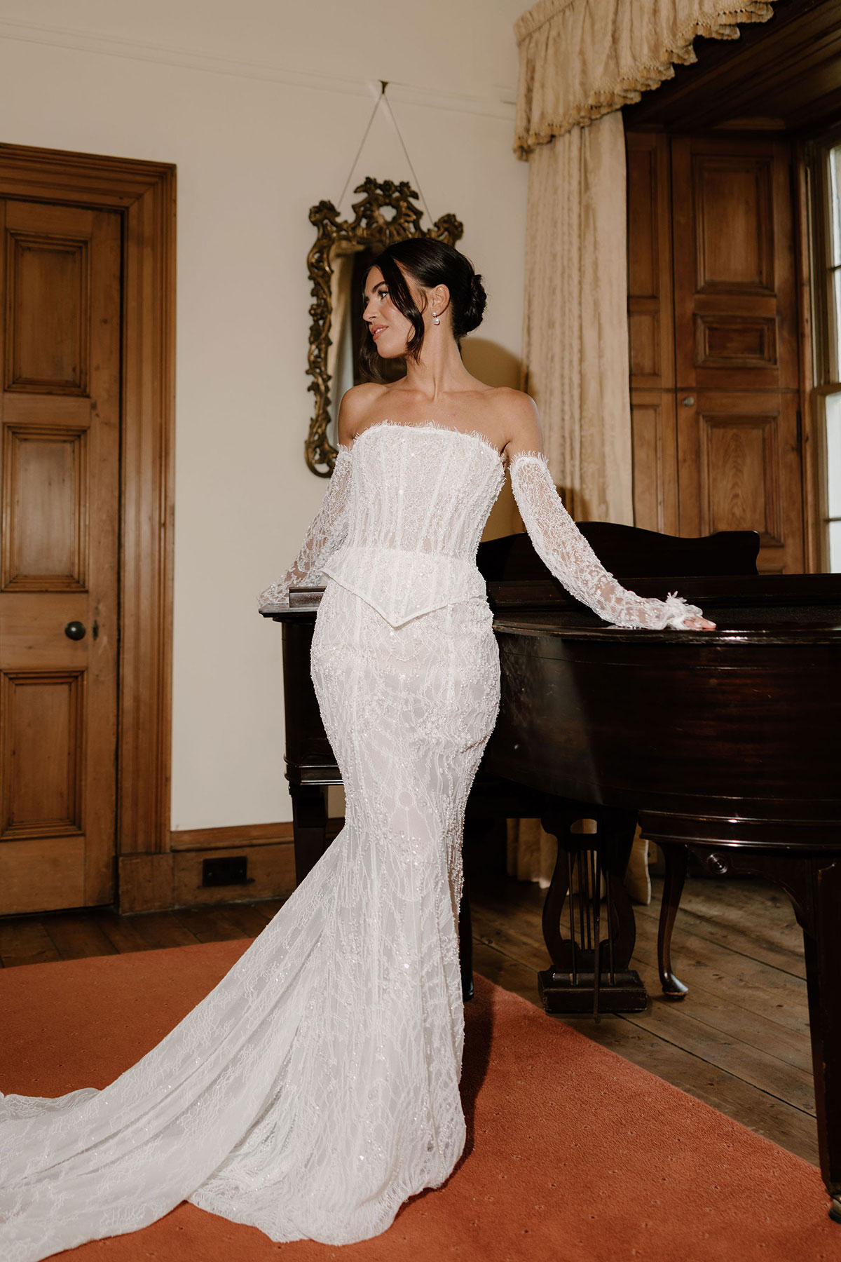 Bride in an embellished off-the-shoulder wedding gown posing beside a grand piano