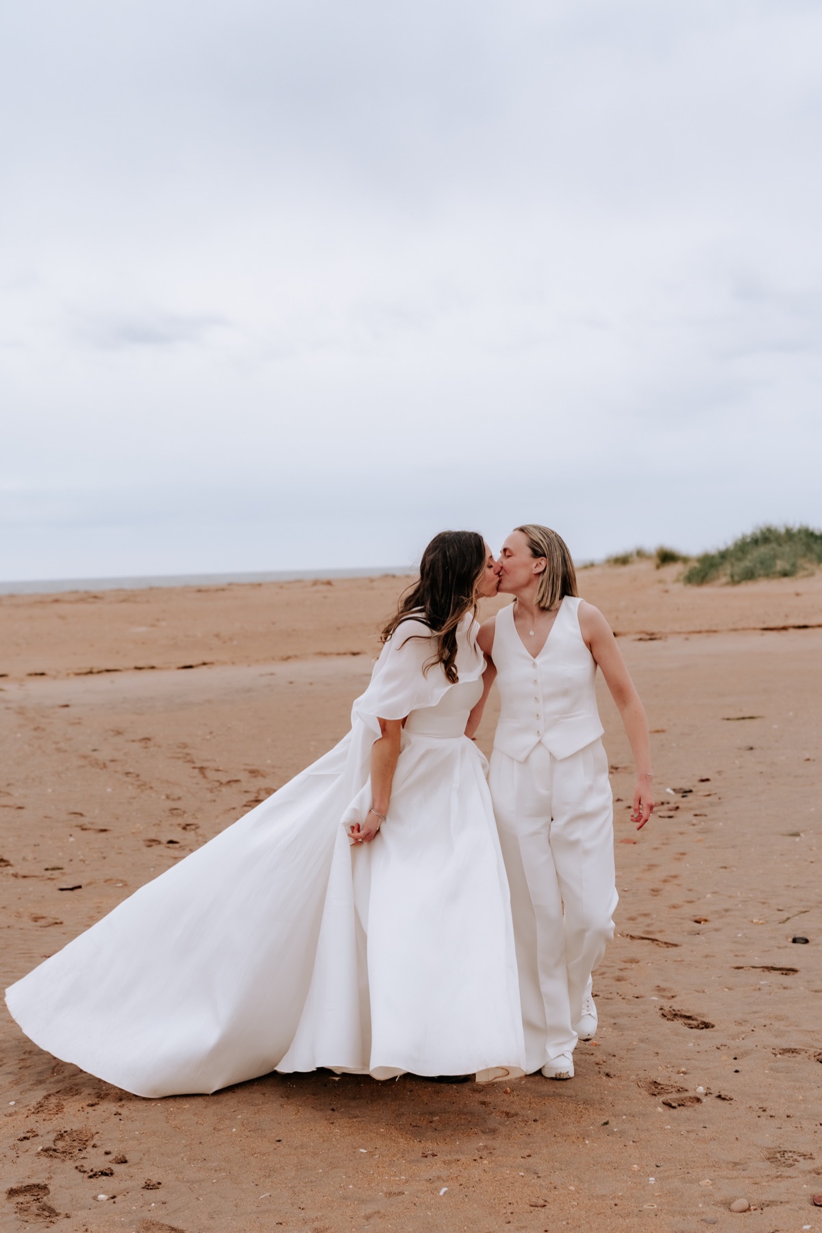 Hannah and Donna kissing while walking together on the beach after their Harvest Moon wedding.