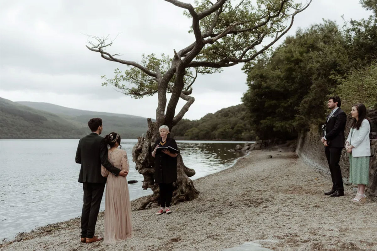 couple getting married in front of witnesses and celebrant on beach next to water