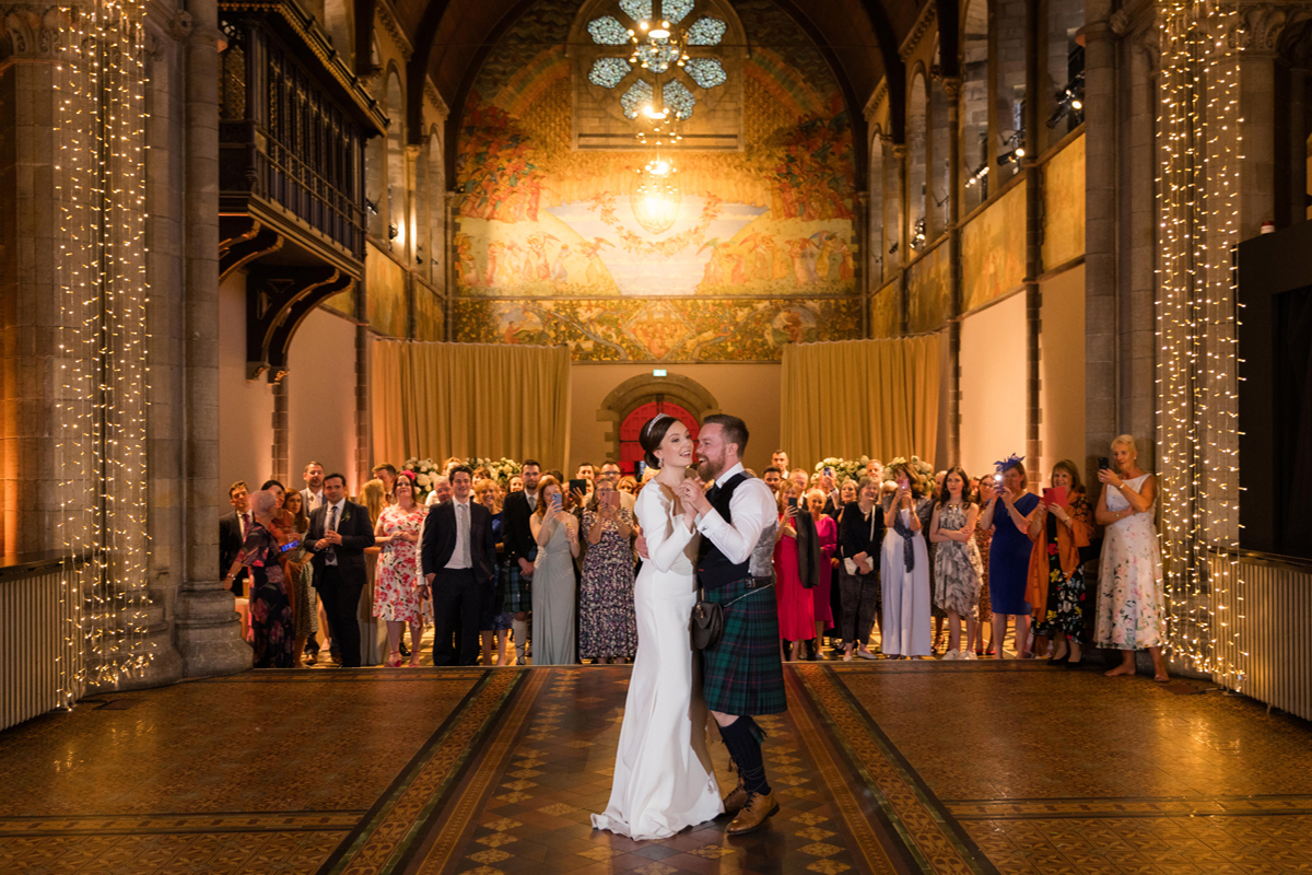 Couple sharing their first dance surrounded by guests inside Mansfield Traquair with illuminated murals and arches