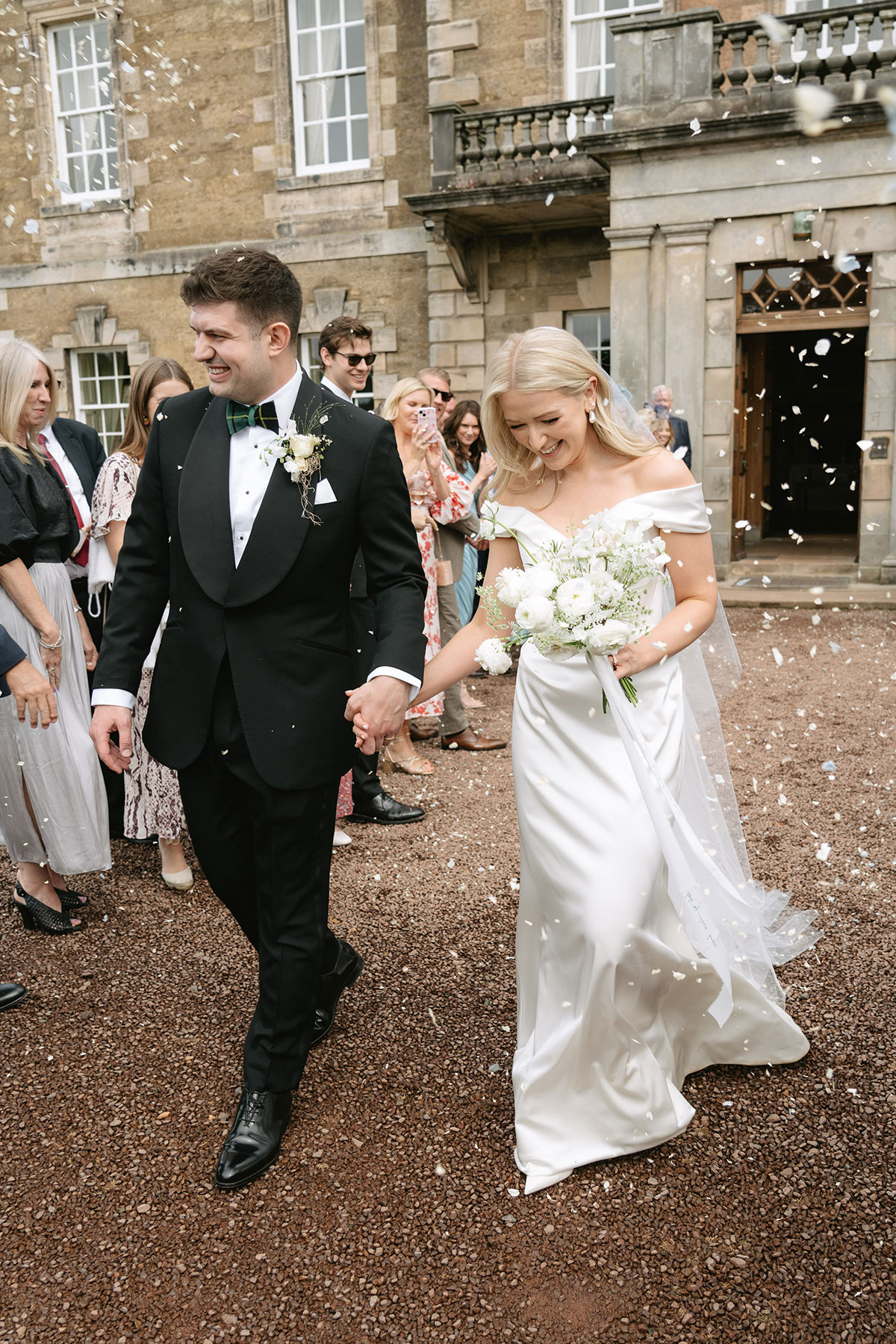 Bride and groom walking through confetti outside Gilmerton House wedding venue East Lothian
