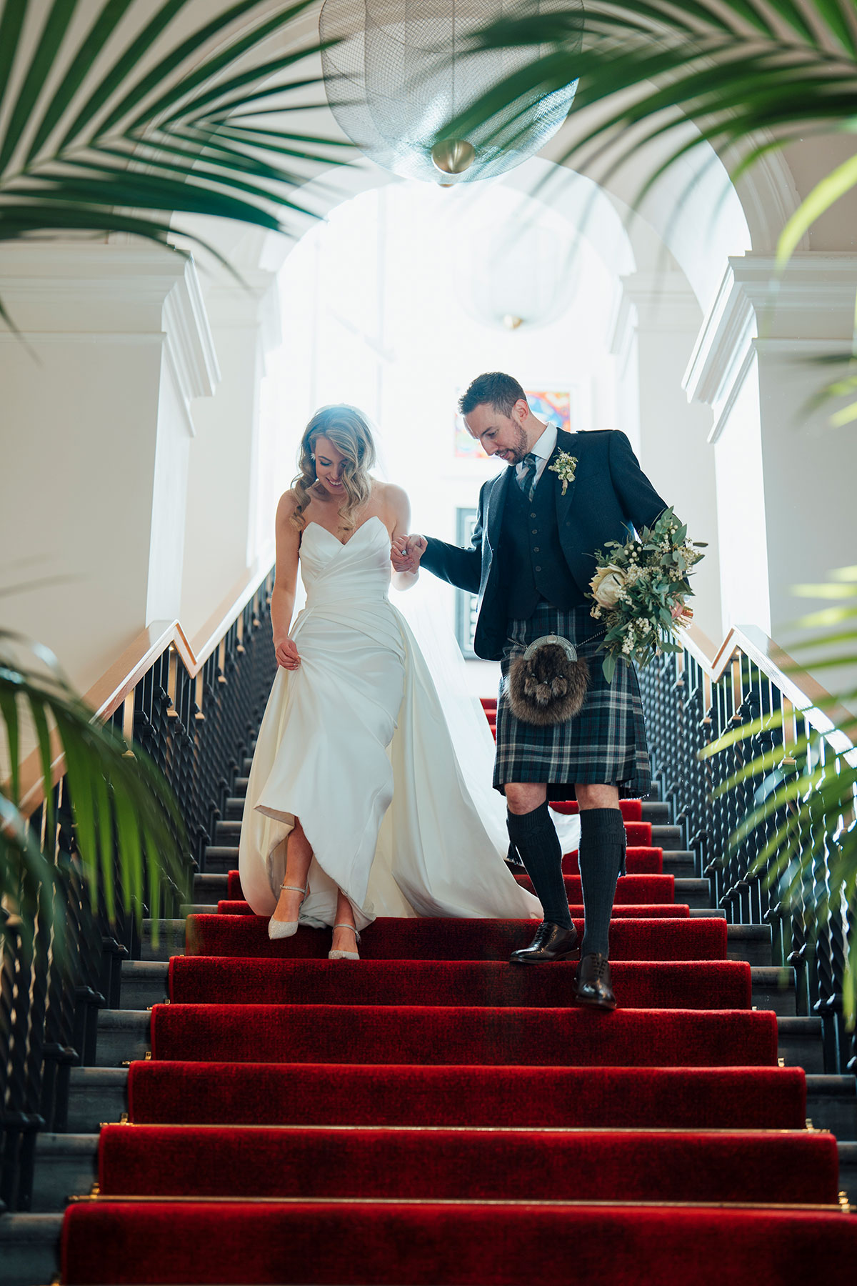 couple walk down red carpet stairs during wedding at Virgin Hotels Edinburgh