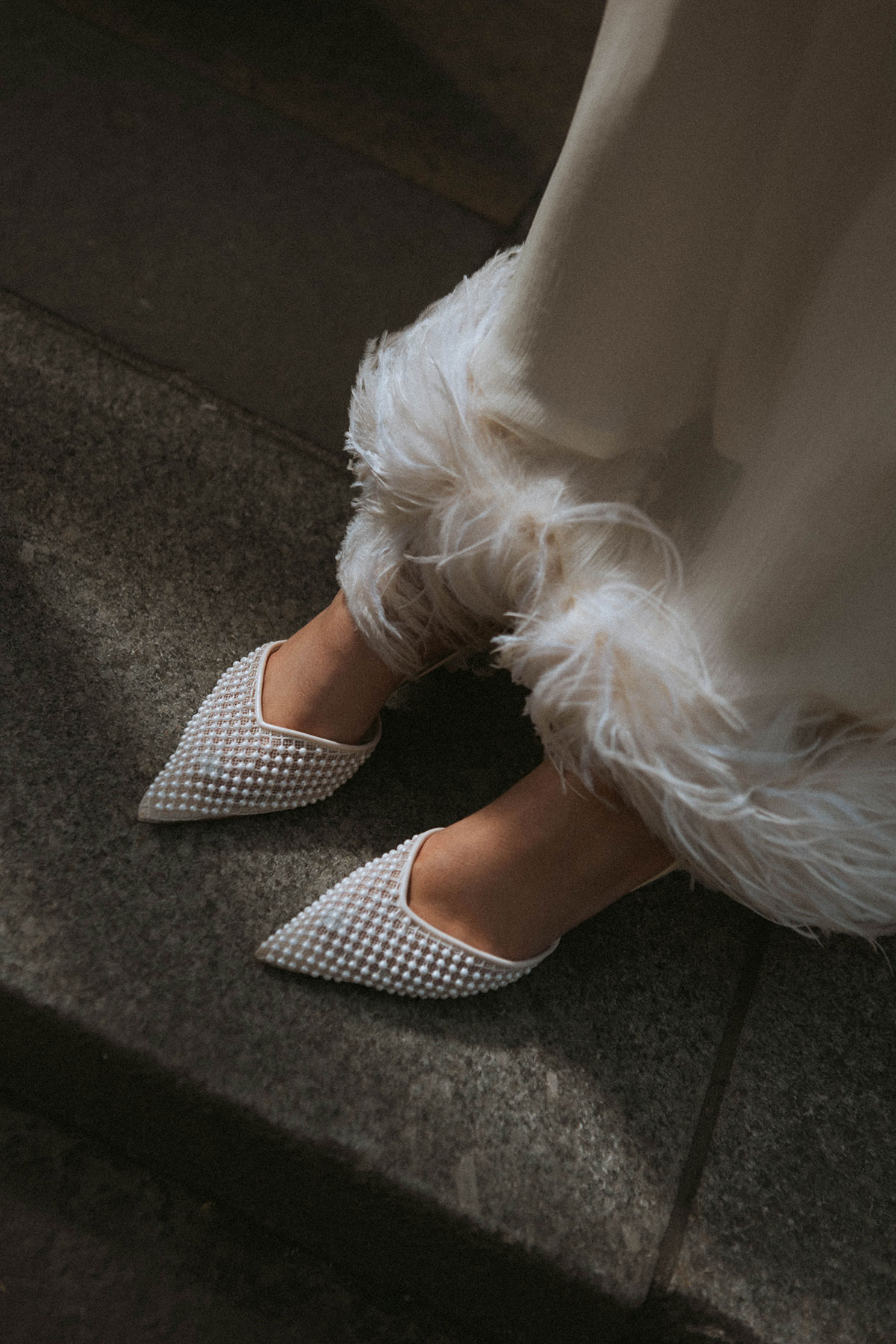 Close-up of pearl bridal shoes and feather-trim wedding outfit