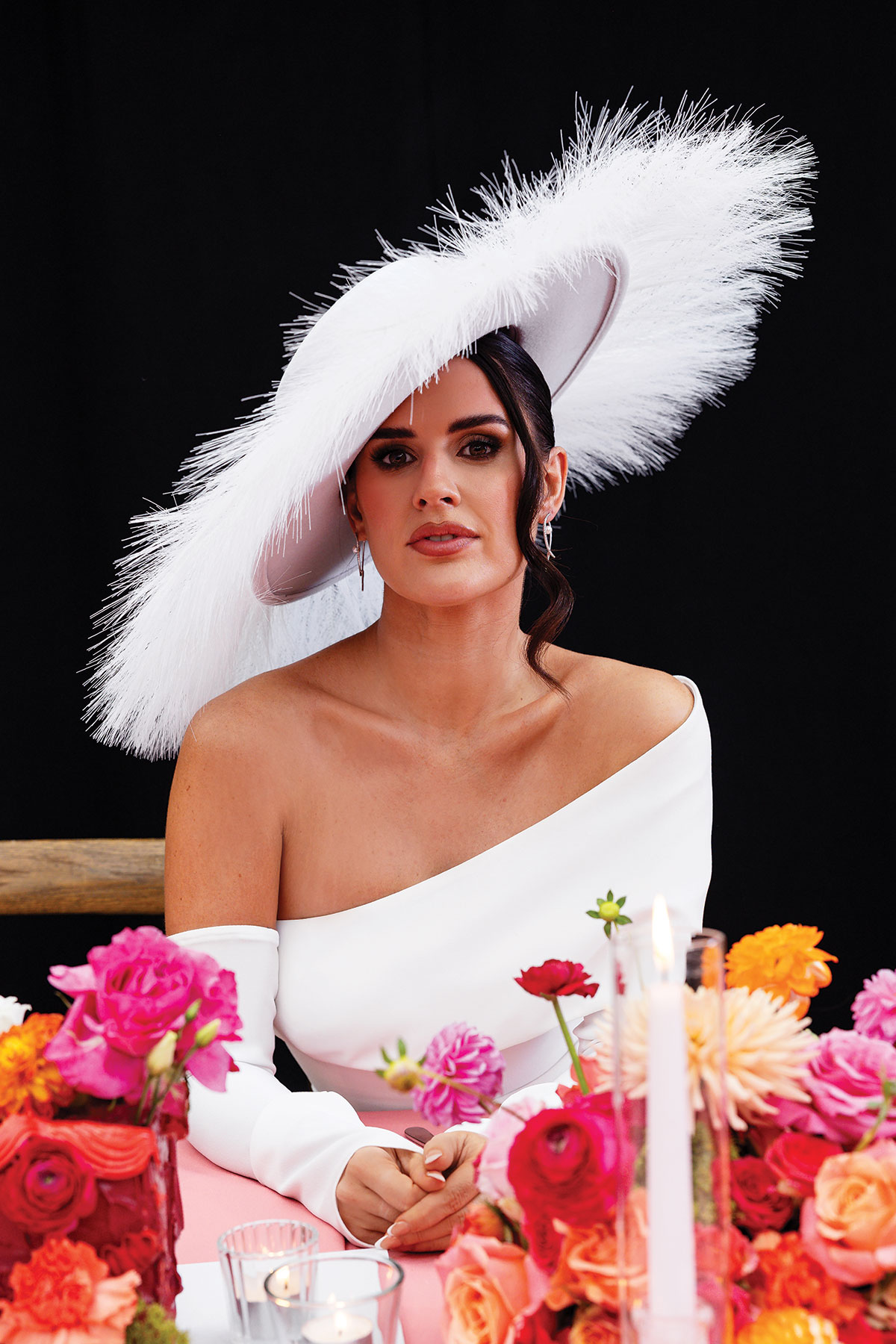 Bride wearing statement white hat and asymmetric dress at bold floral wedding tablescape shoot