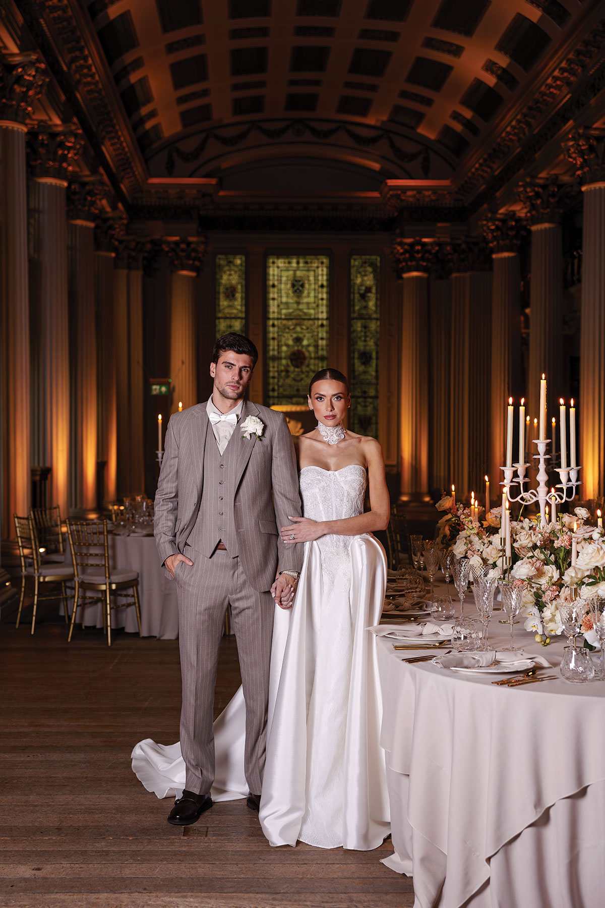 Bride and groom in formal weddingwear posing beneath grand columns and candlelight at Signet Library