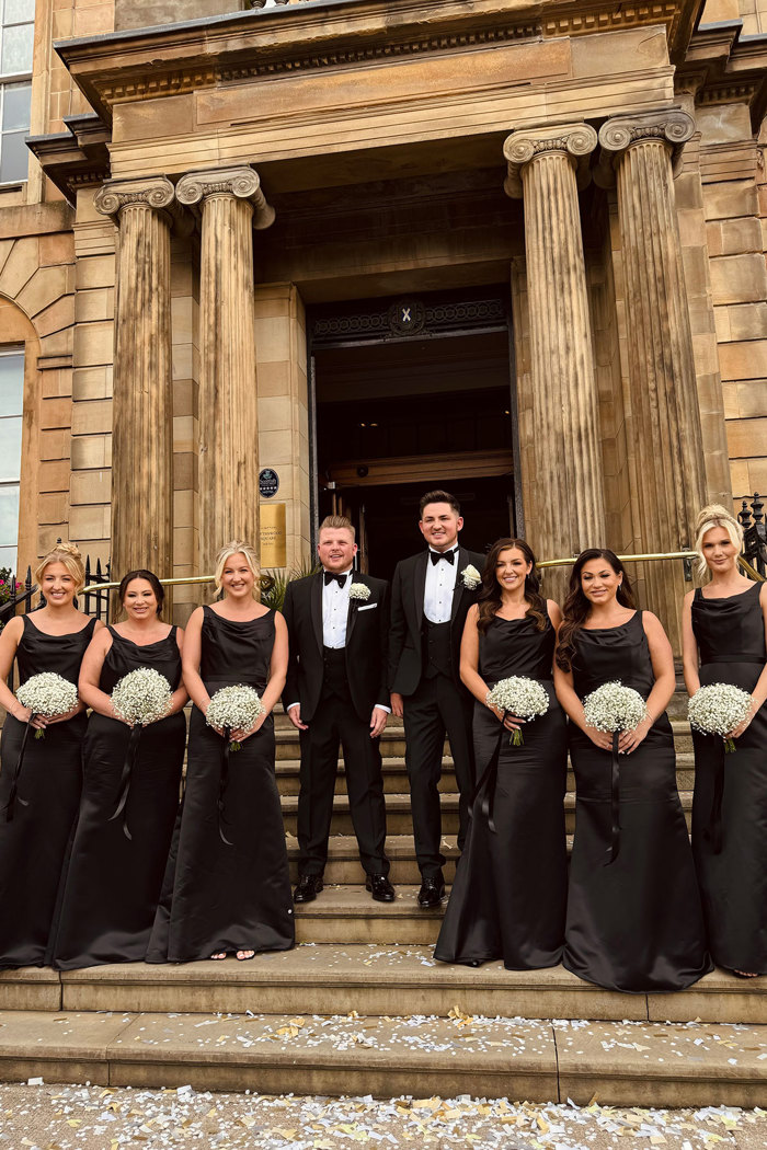 two grooms stand with bridesmaids wearing black dresses on steps at kimpton blythswood square glasgow
