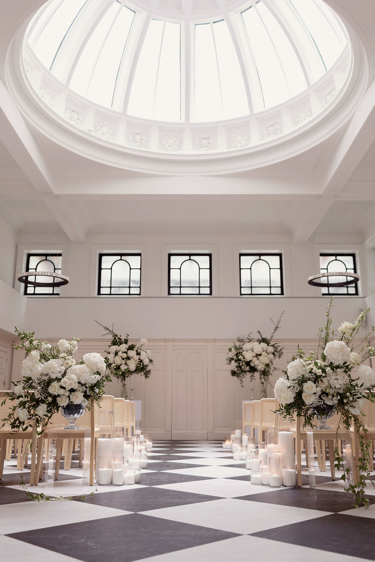 Light-filled wedding ceremony space at The Collector’s Hall in Glasgow, featuring a domed ceiling, black and white floor and floral aisle styling.