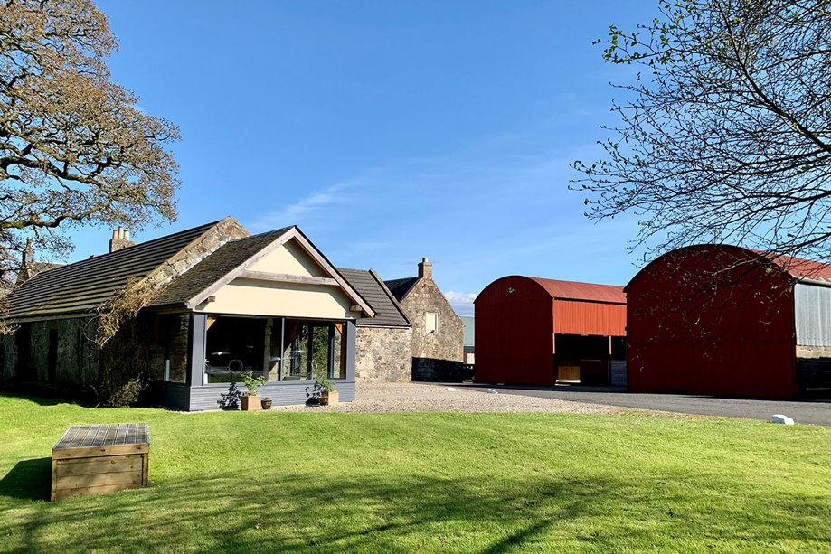 a small stone and glass building on the left with two large red barns on the right on a sunny day