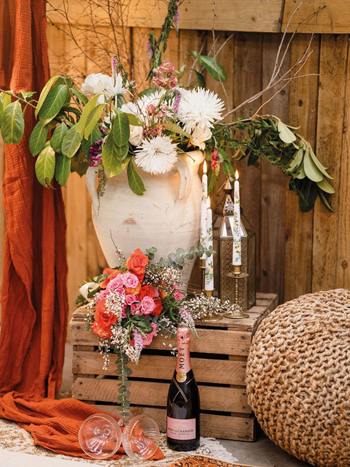 a wooden crate, bottle of champagne and glasses, candlesticks and floral arrangement in a display of red, pinks and orange