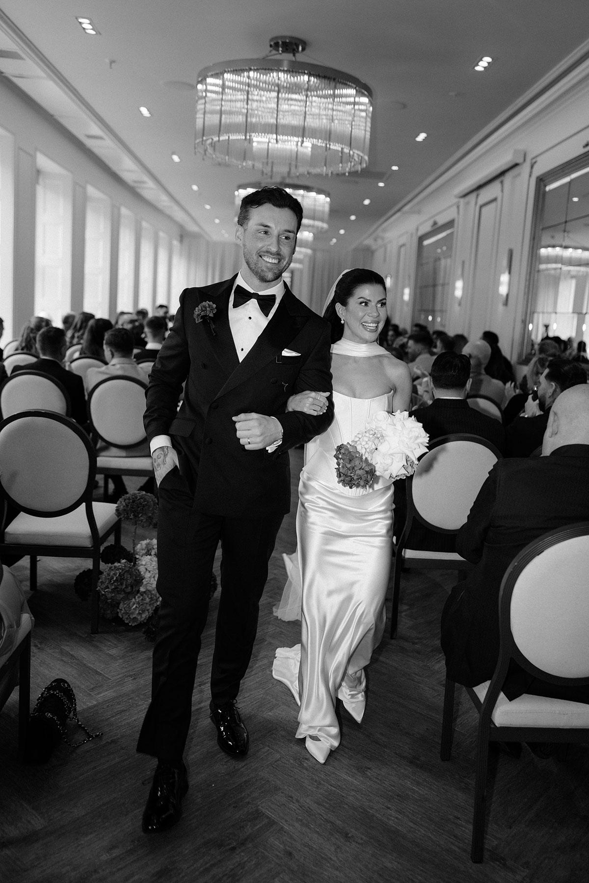 Newlyweds walking back up the aisle after their ceremony at The Exchange Glasgow, smiling with guests seated behind