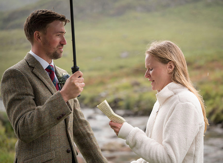 a bride reading vows to a groom as they stand under an umbrella