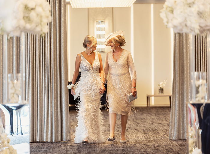 two older women wearing glamorous gowns and holding hands entering a neutrally decorated room at Lochside House Hotel