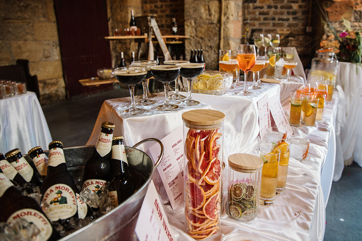 Wedding cocktail station with espresso martinis, aperol spritzes, citrus garnishes and bottled beer set up inside Kinkell Byre's rustic barn.