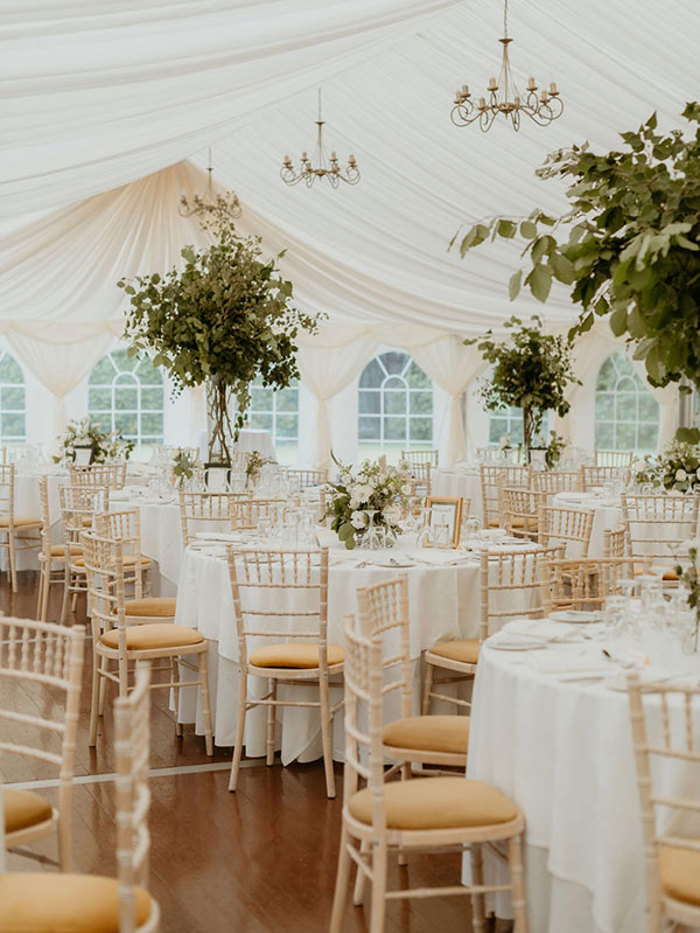 a flowy white marquee set up with white linens, round tables and lots of greenery