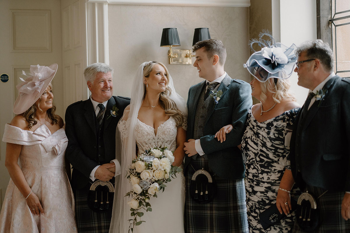 bride and groom smile at one another as their families stand at either side of them