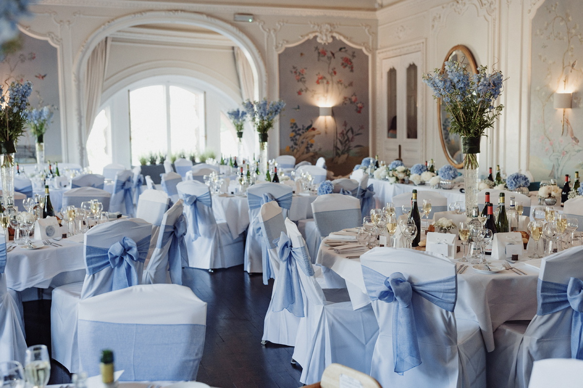 Blue and white wedding reception décor with floral centrepieces and chair sashes at Dean Banks, The Caledonian