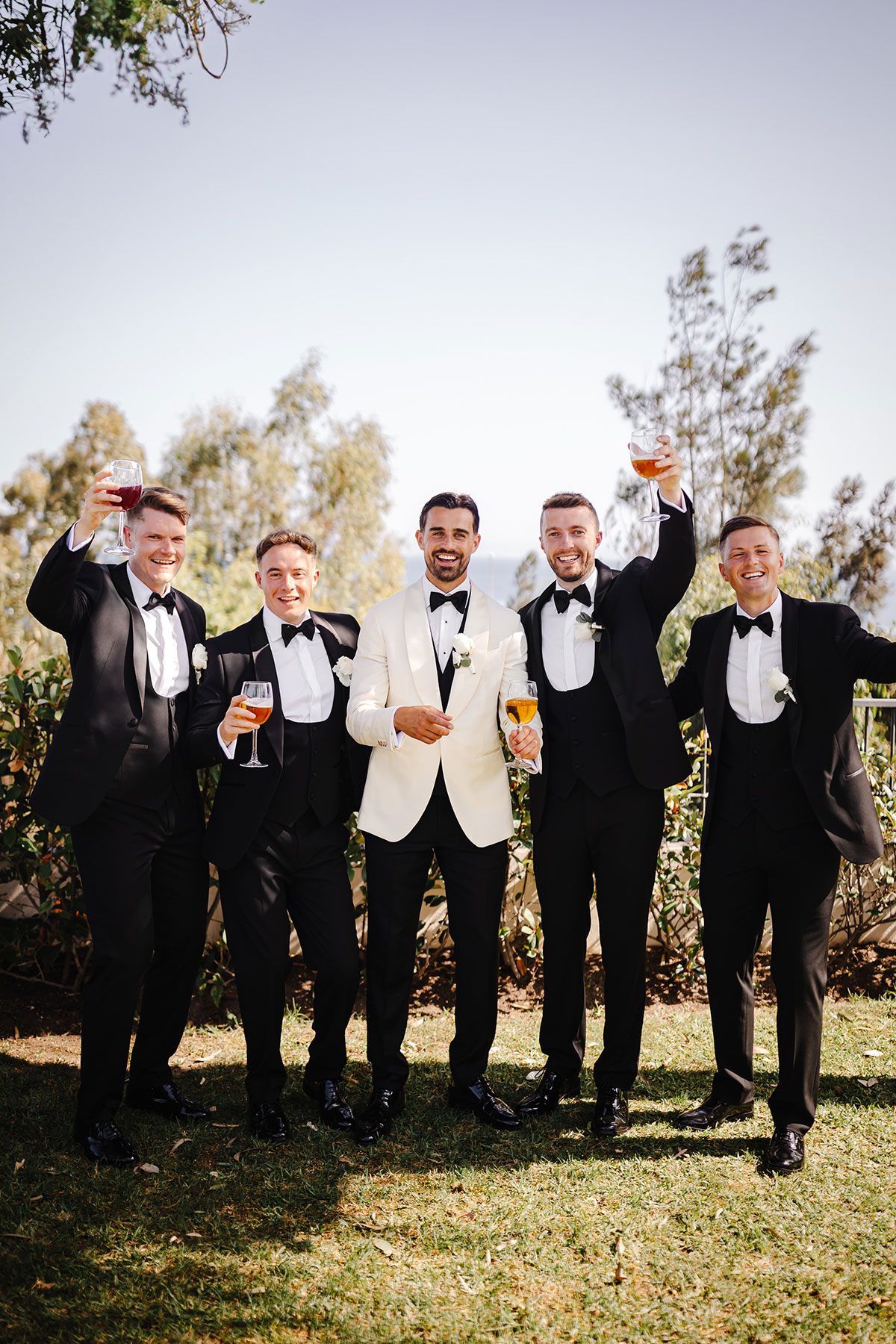 Groom and groomsmen in tuxedos raise glasses for a celebratory toast