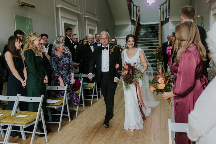 Bride Walking Down Aisle At Netherbyres House With Man In Black Tuxedo As Guests Look On