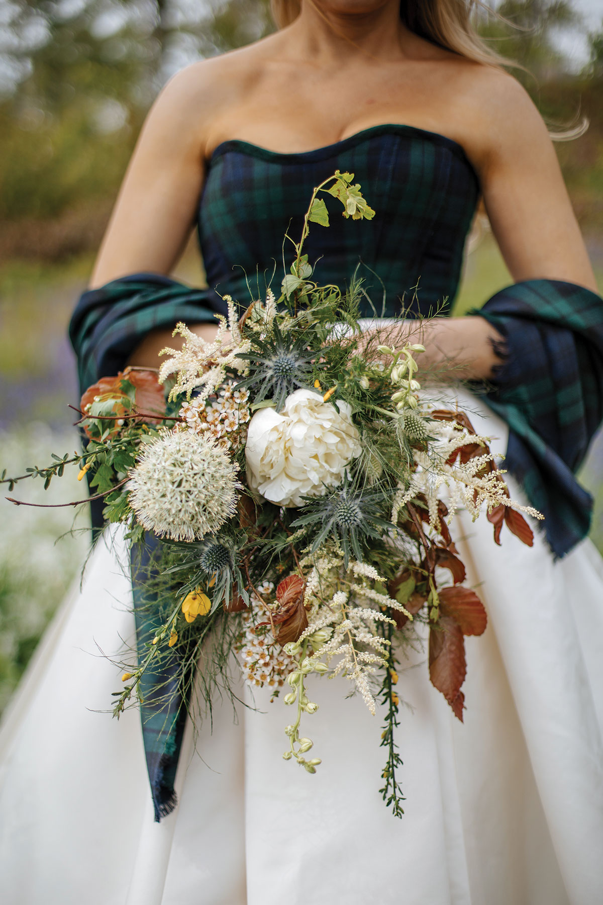 Bride wearing a dark green and navy tartan corset and matching wrap while holding a wildflower bouquet.