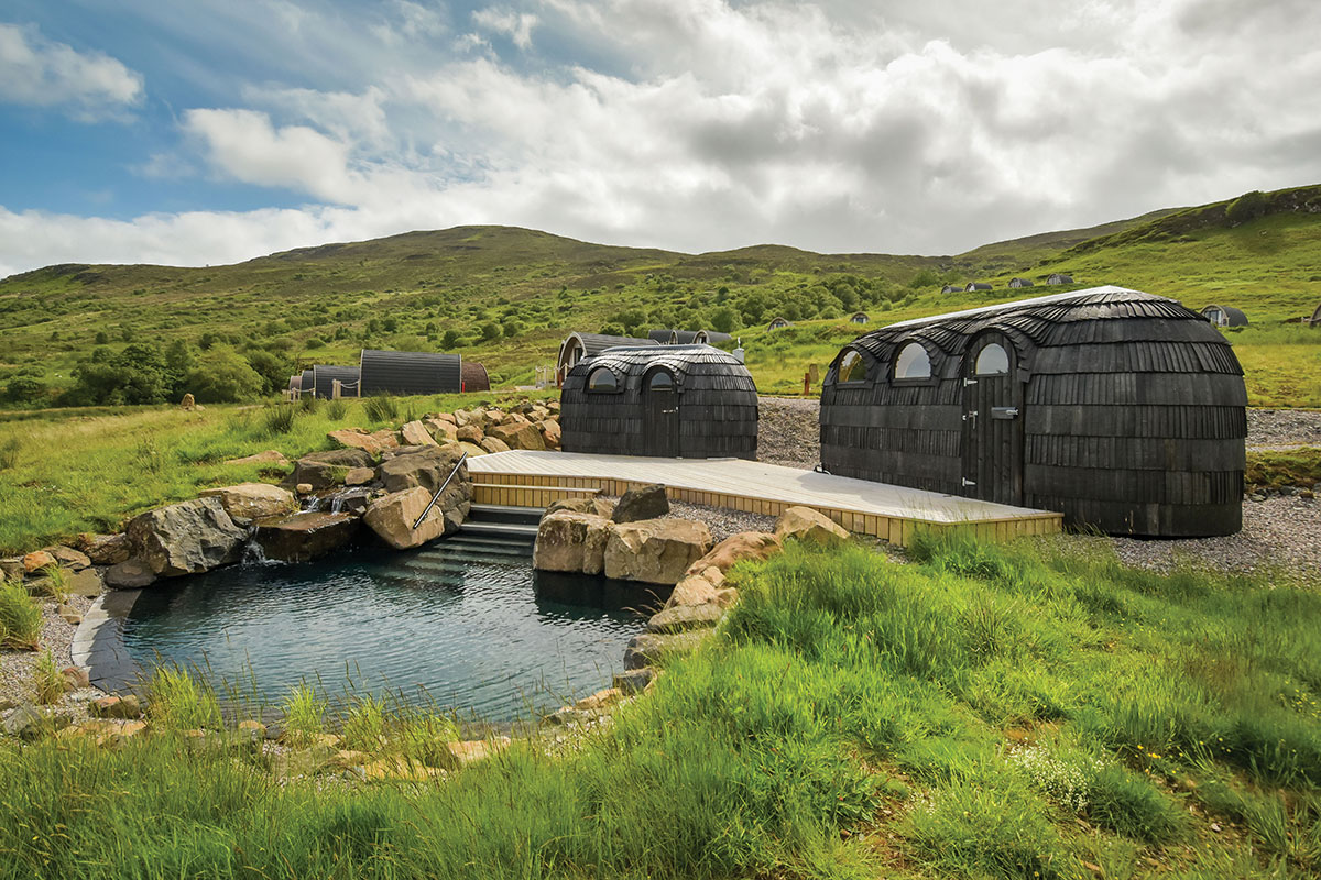 Outdoor spa pool and black timber cabins at Bracken Hide on the Isle of Skye, surrounded by rolling Highland hills