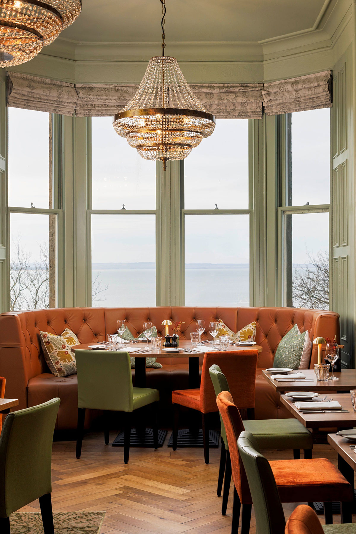 Elegant dining space at Hotel du Vin St Andrews with leather banquette seating, chandeliers and panoramic views over the coastline through large bay windows