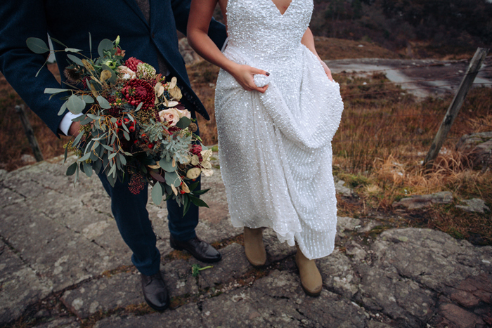 Image showing groom holding bride's flowers and bride walking in brown boots holding up her dress