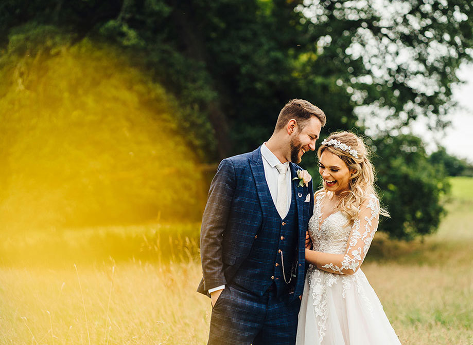Bride and groom couple laugh, holding onto each other in a field of grass