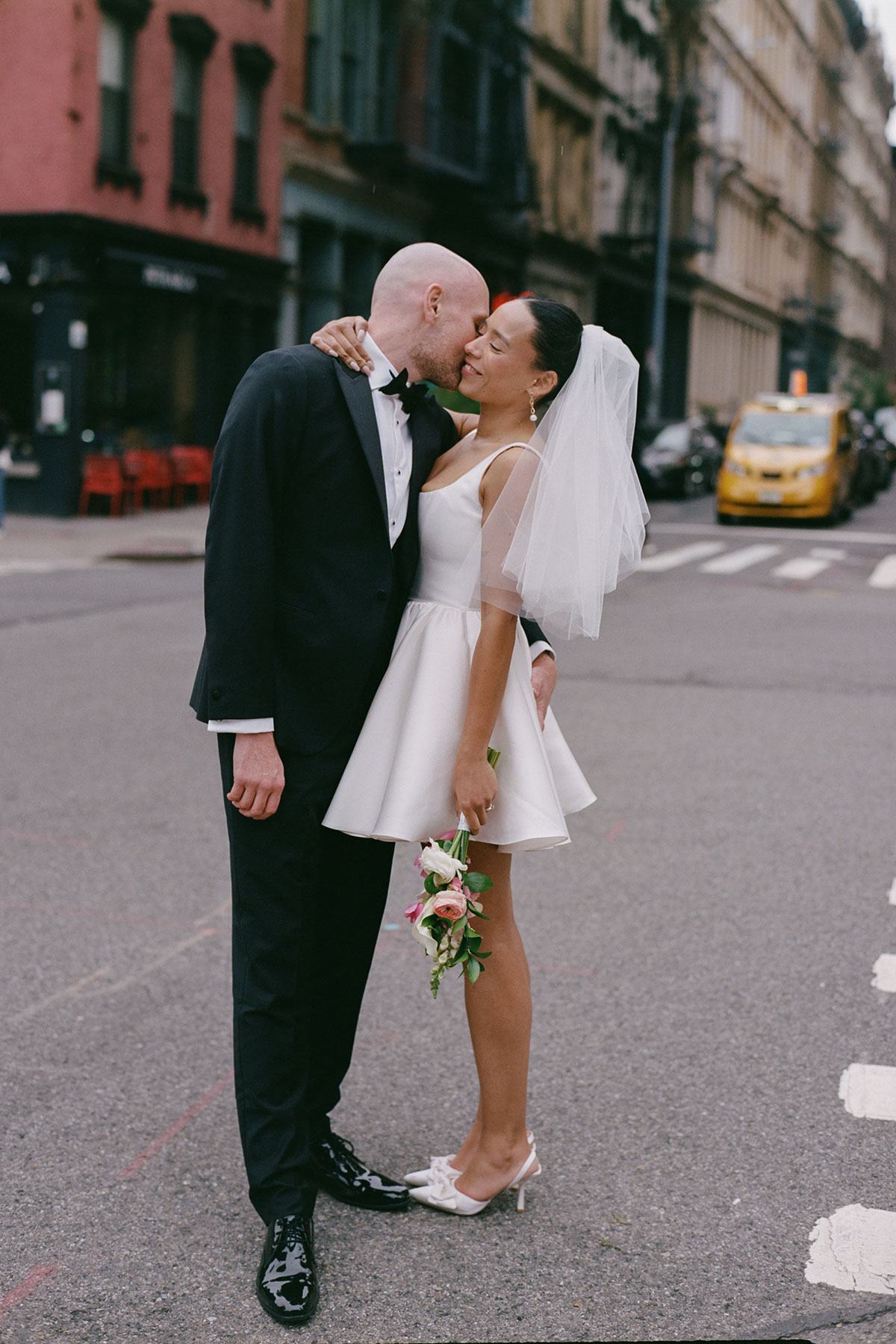 Bride in short wedding dress and veil kissing groom on New York city street with bouquet