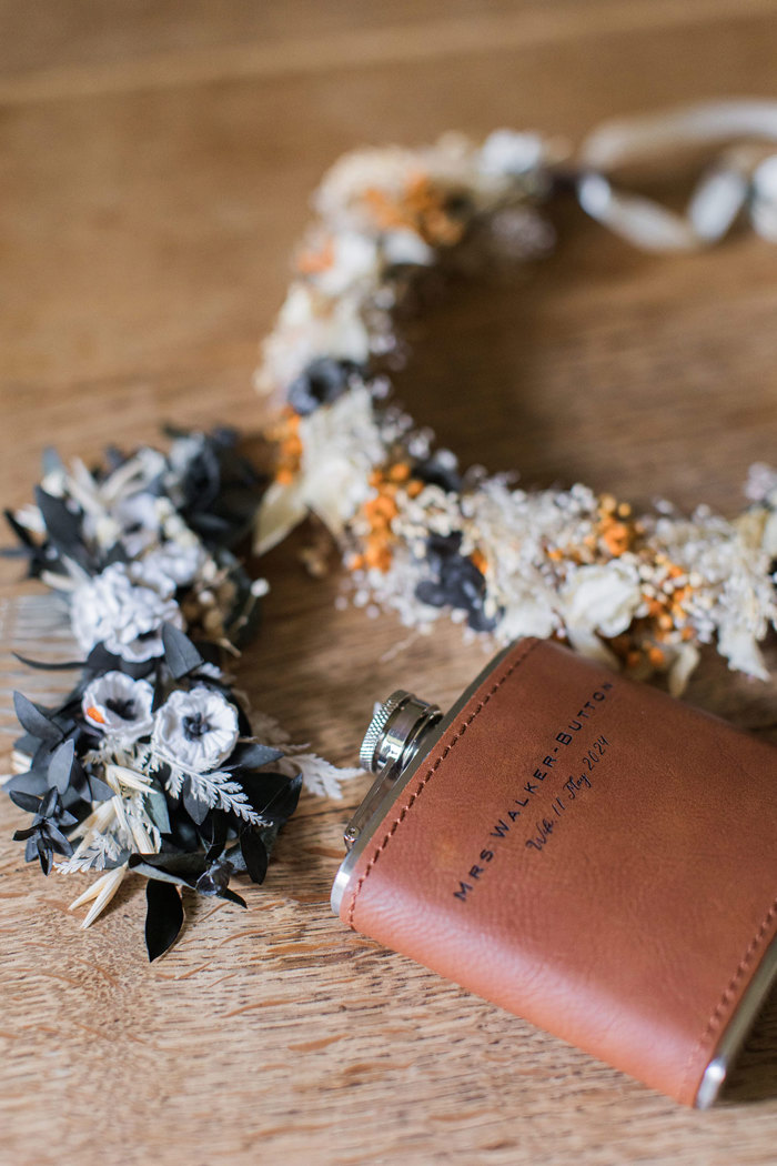 details of a brown-red leather hipflask and dried flower crown on a wooden surface