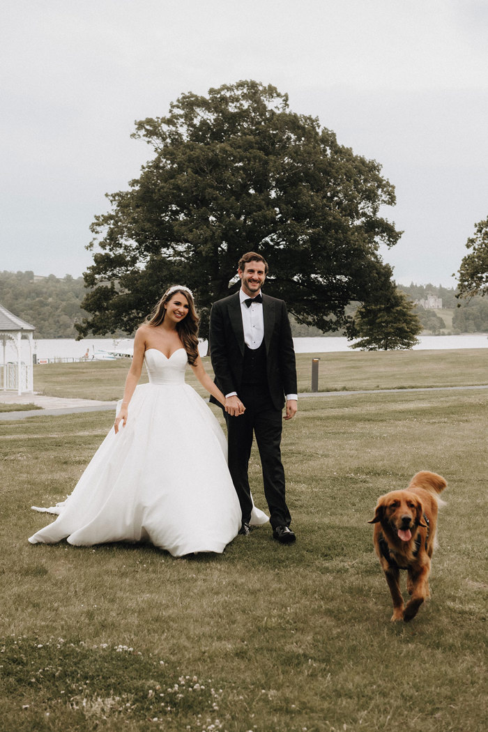 a bride and groom walking in the grounds of Cameron House with their dog.