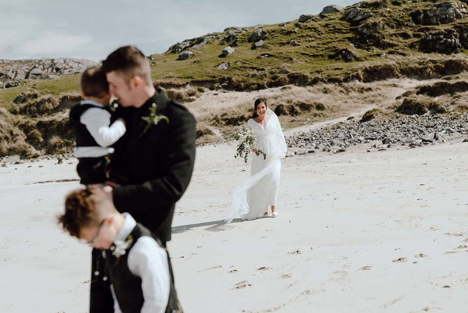 Bride walks towards groom and children for first look on beach