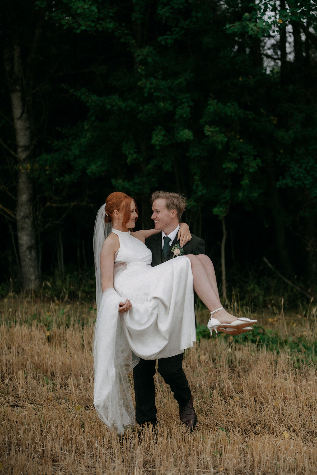Groom lifting bride in harvested field during countryside wedding portraits