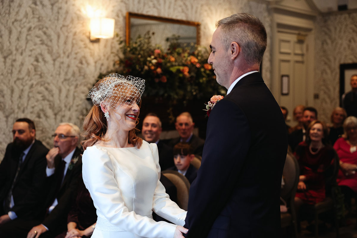 a bride and groom smiling at each other as guests look on