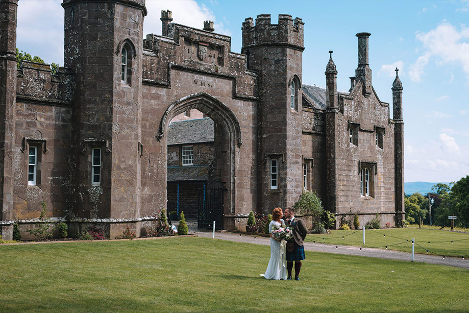 A bride and groom standing on the lawn outside a castle