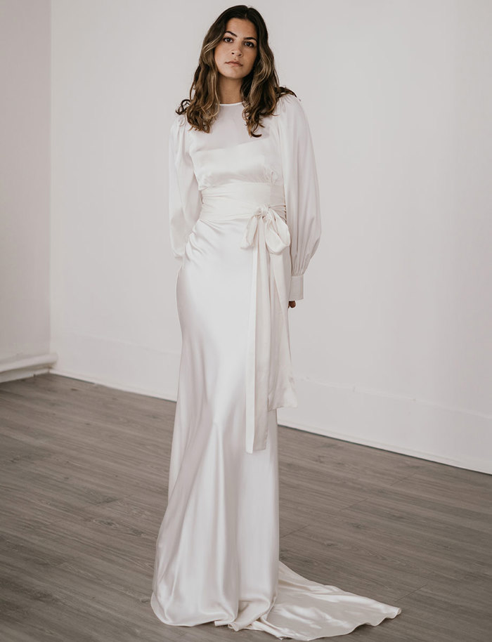 brunette woman wears a tie front long sleeve top over a floor-length silky white gown