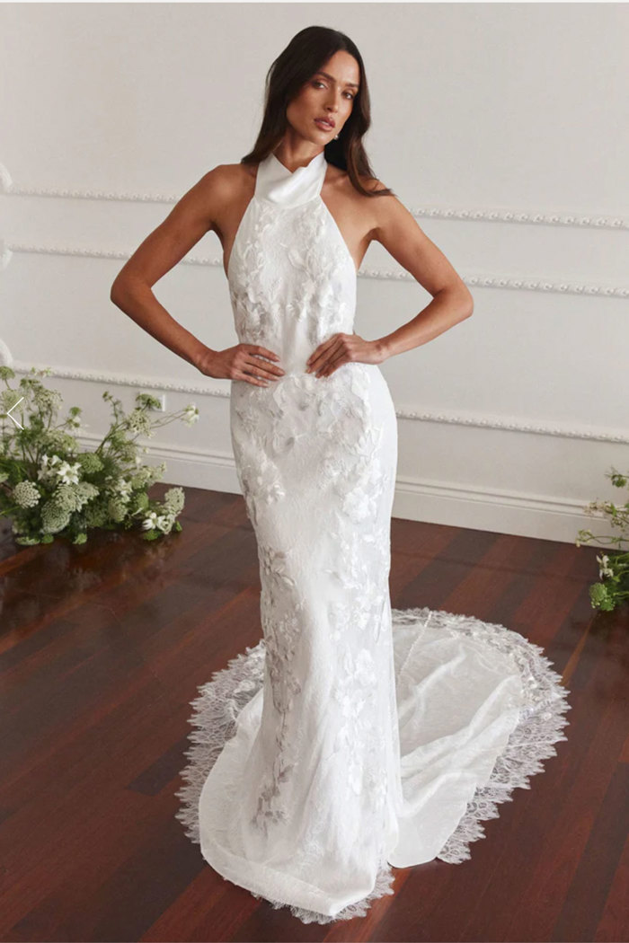 brunette model wears white halterneck wedding dress with floral embroidery and lace bordered train