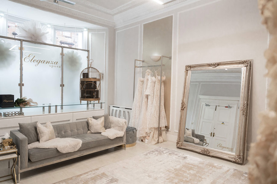 view of a room in Eleganza Sposa, with long grey sofa on one side and a large rectangular mirror propped up on the floor on the other on the other side