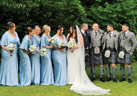 Five bridesmaids in blue, bride, groom and three groomsmen standing in row