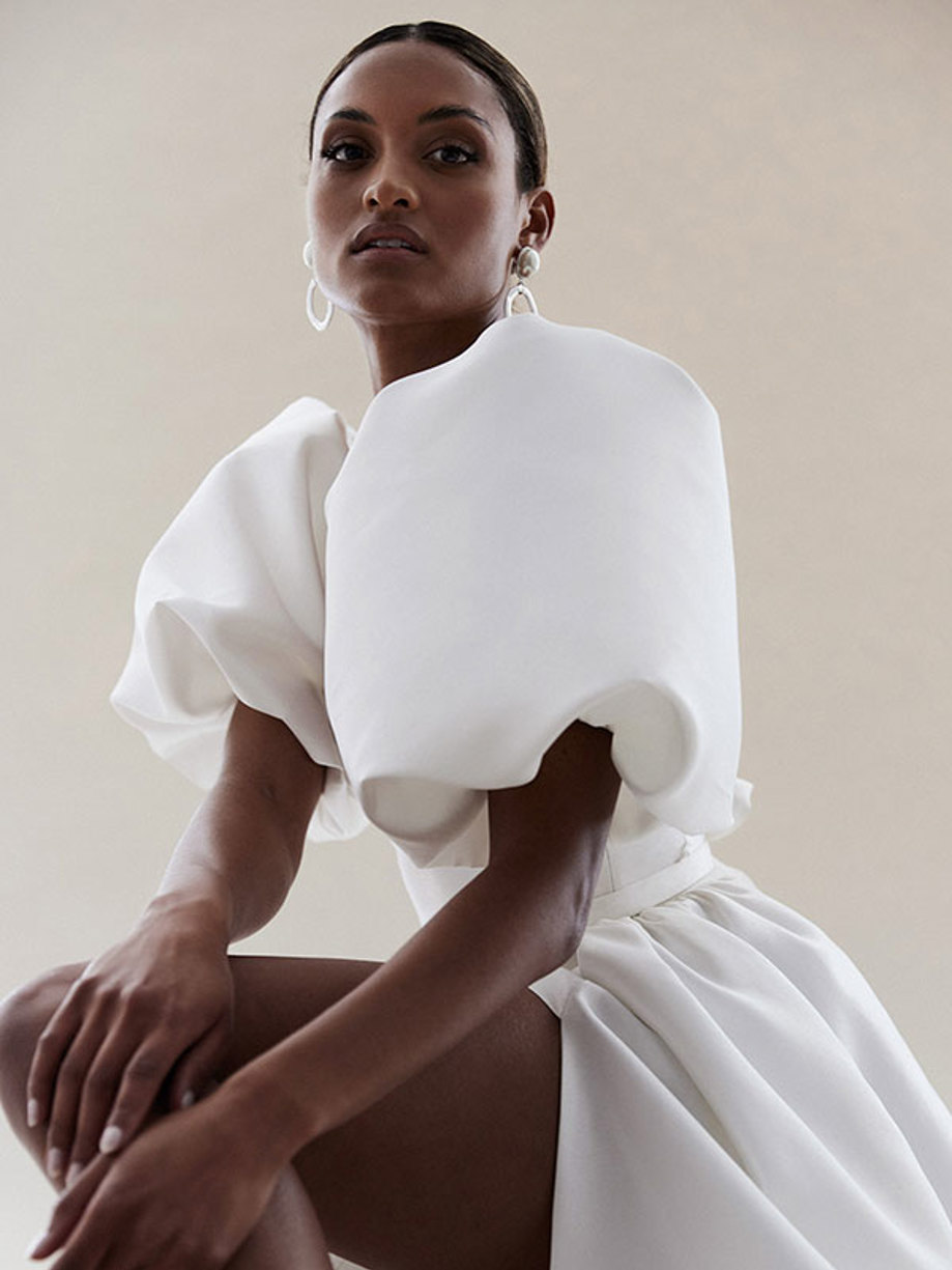 woman crouches down in white leg slit wedding gown with very large puff sleeves facing side on to the camera