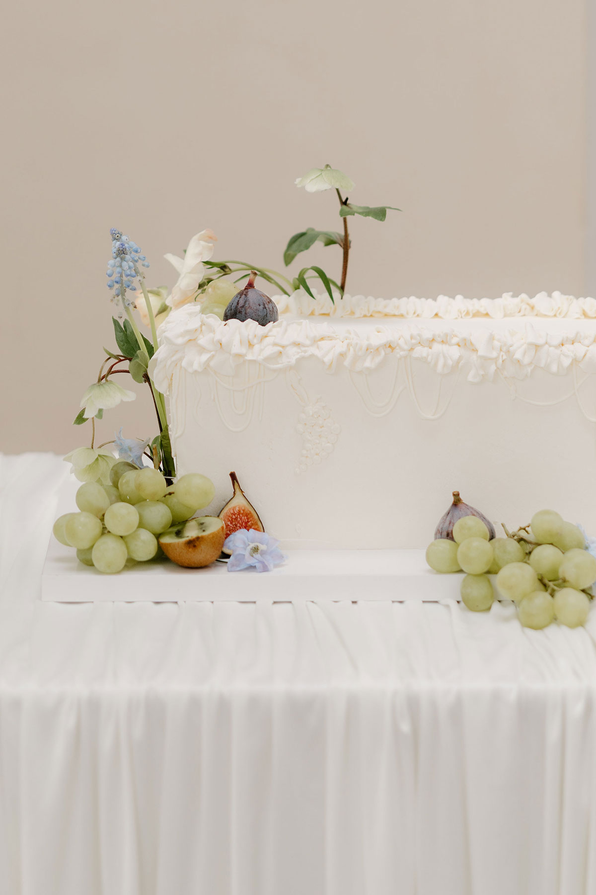 White wedding cake decorated with flowers, grapes and figs