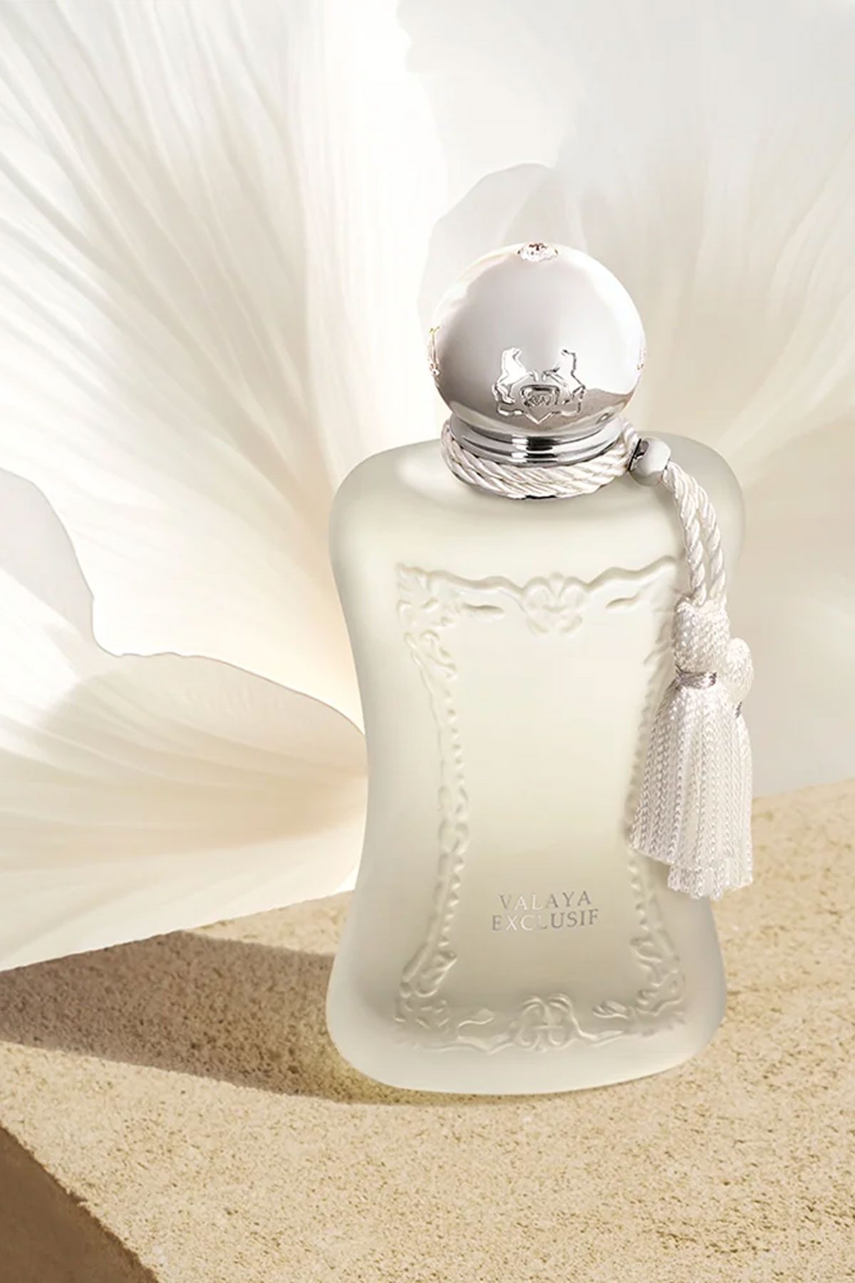 Parfums de Marly Valaya Exclusif fragrance bottle with silver cap and tassel against a soft cream floral backdrop.