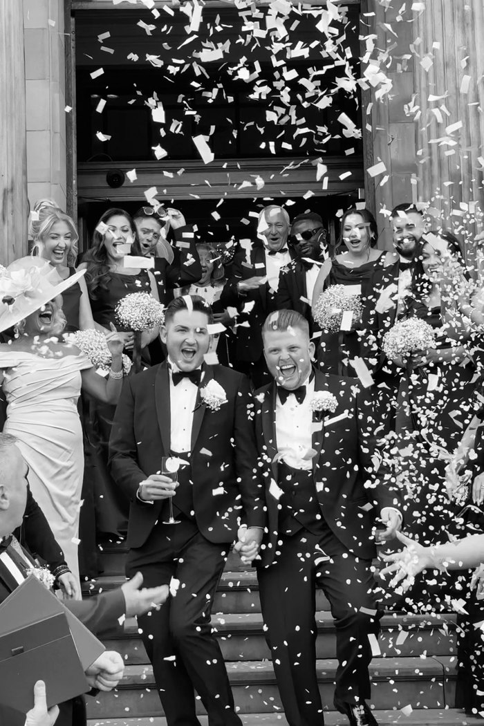 black and white picture of grooms smiling as guests throw confetti over them on steps of kimpton blythswood square