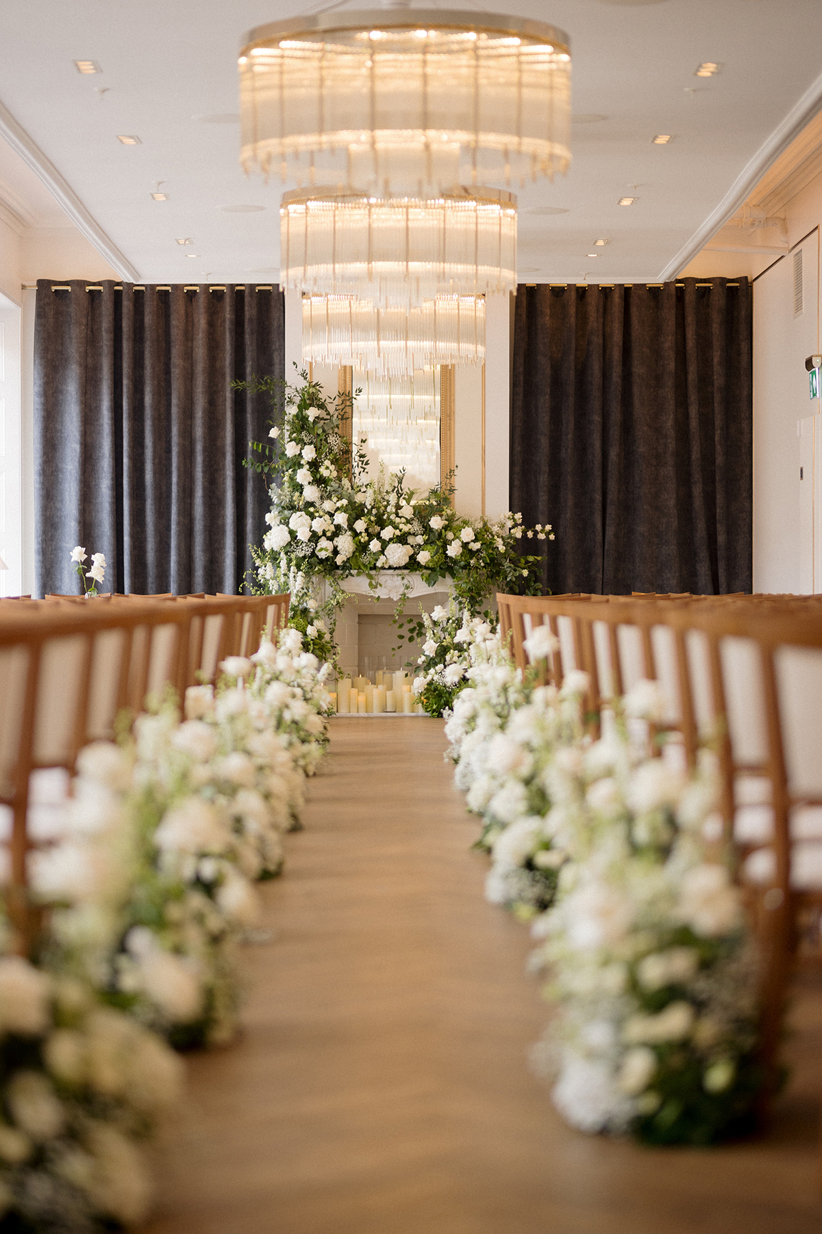 Wedding ceremony aisle lined with white flowers leading to a fireplace floral backdrop