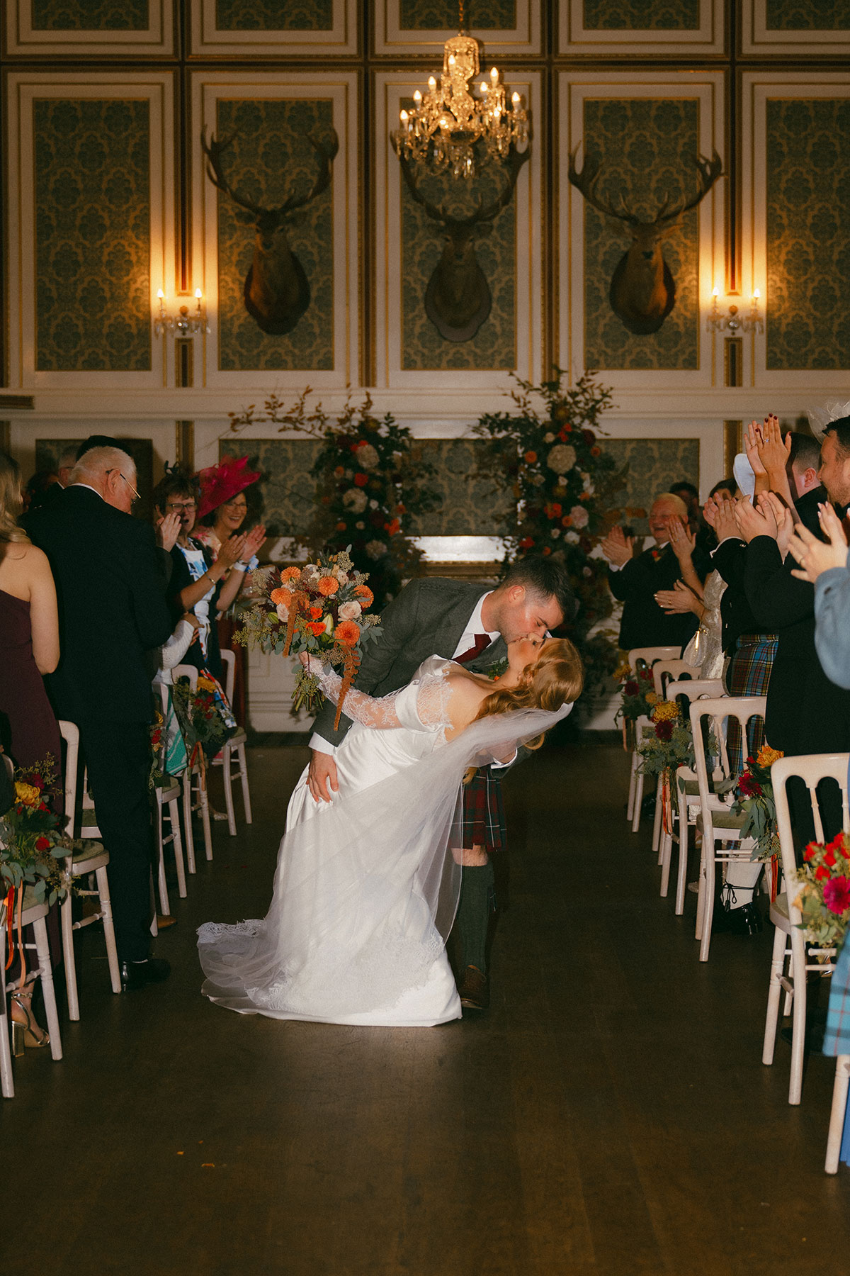 Bride and groom sharing first kiss at the end of their Scottish wedding ceremony surrounded by guests and florals
