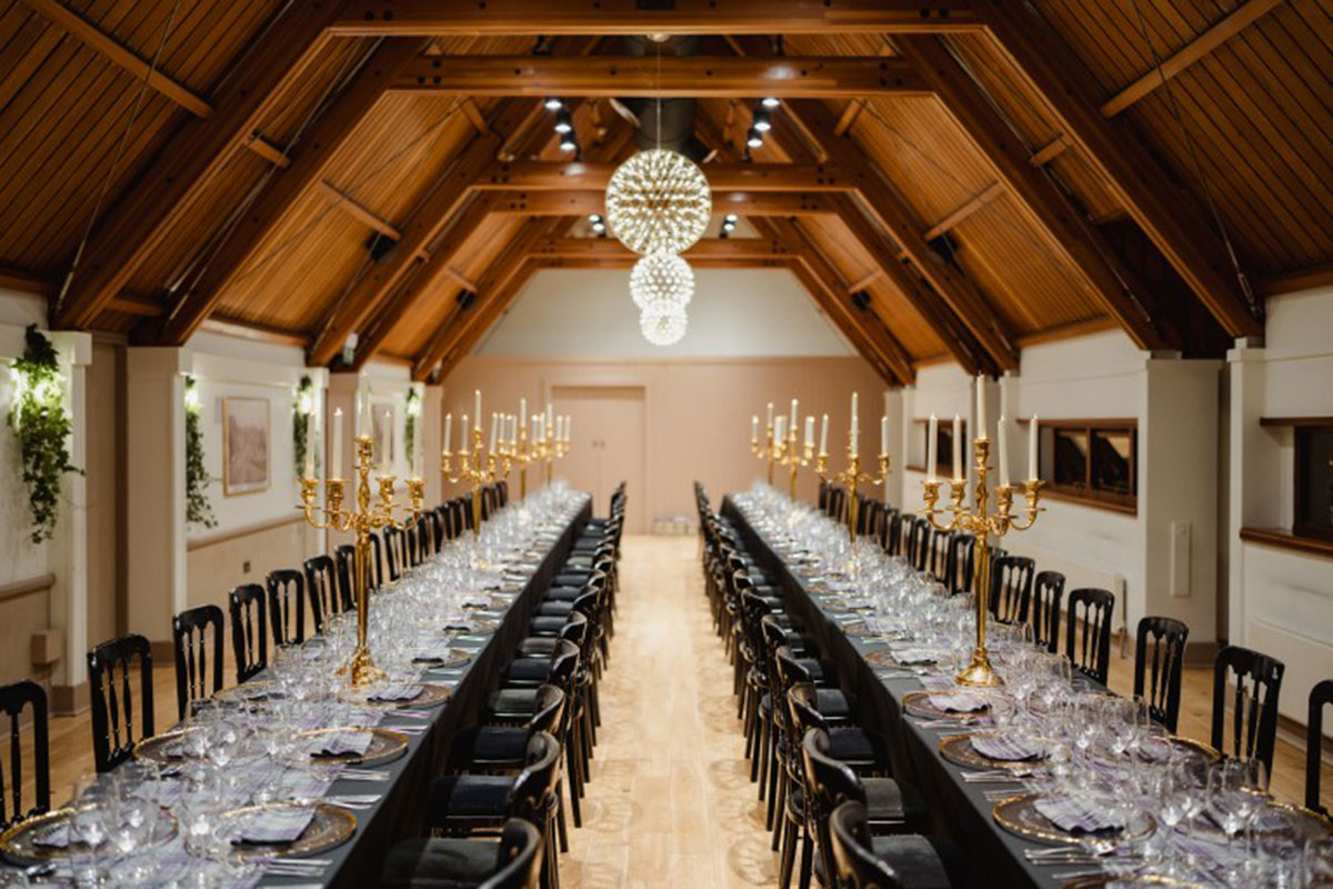 Long banquet tables dressed for a wedding breakfast at Edinburgh Castle, complete with gold candelabras beneath the timber-beamed ceiling